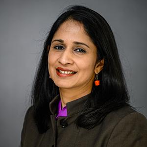 A woman with dark, straight hair, wearing a black jacket and dangling orange earrings