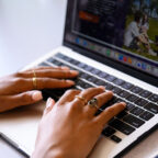 Hands wearing pinki nail polish and a Clemson ring rest on a laptop keyboard.