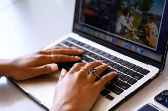 Hands wearing pinki nail polish and a Clemson ring rest on a laptop keyboard.