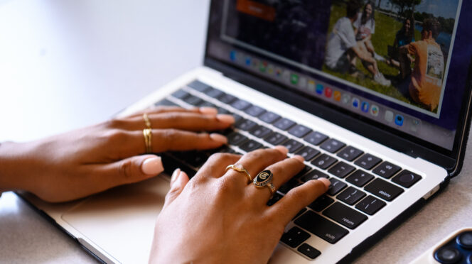 Hands wearing pinki nail polish and a Clemson ring rest on a laptop keyboard.