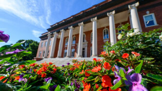 Low-angle view of Clemson University’s Sikes Hall framed by colorful orange and purple flowers under a bright blue sky.