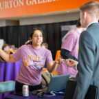 A female in a t-shirt gives instructions to a male in a suit