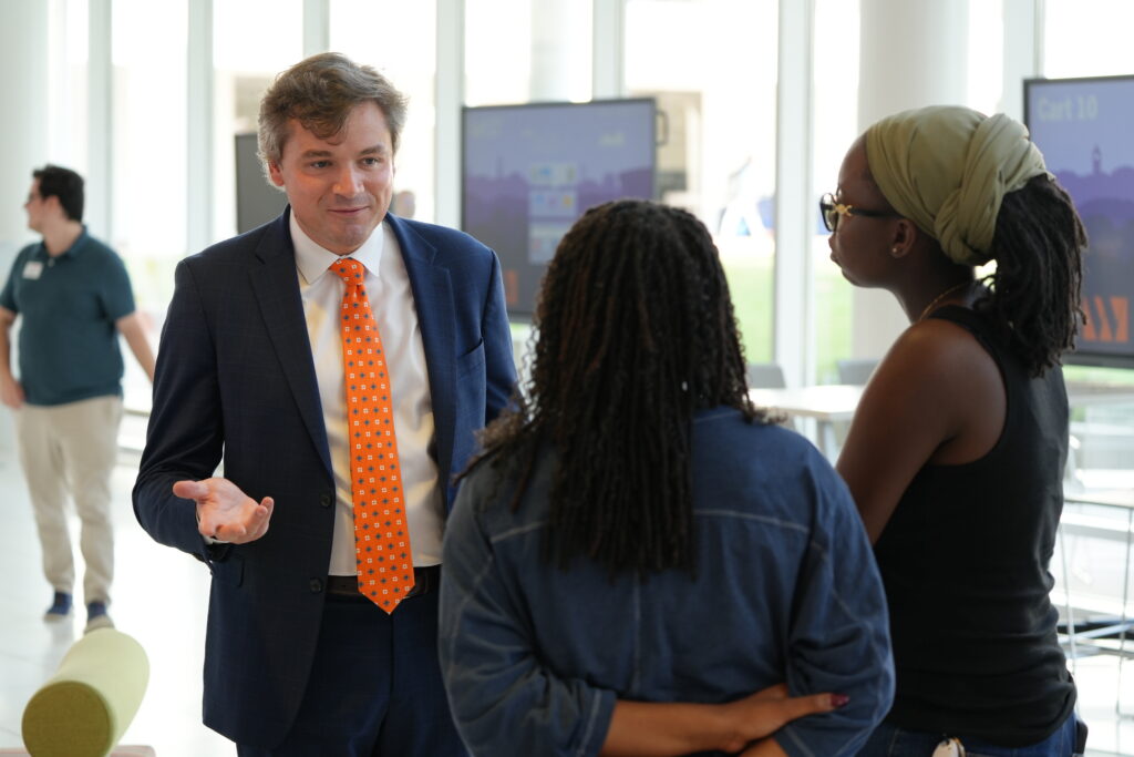 A man in suit with an orange tie speaks to two students