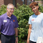 A male in glasses wearing a purple polo shirt speaks to a student wearing a Clemson Home t-shirt