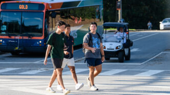 Three males walk across a crosswalk with a CATbus in the background