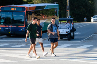 Three males walk across a crosswalk with a CATbus in the background