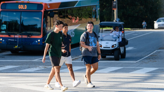 Three males walk across a crosswalk with a CATbus in the background