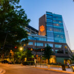 Clemson Greenville One building with an illuminated orange paw logo at a downtown Greenville intersection at dusk.