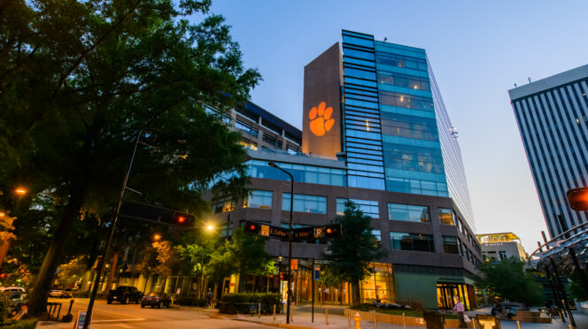 Clemson Greenville One building with an illuminated orange paw logo at a downtown Greenville intersection at dusk.
