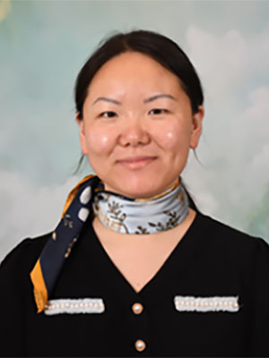A woman with black hair tied into a ponytail, wearing a black shirt and decorative scarf around her neck
