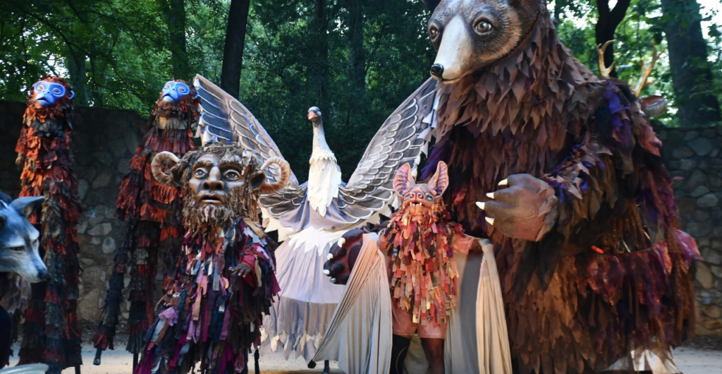 Large-scale puppets of various animals perform on an outdoor stage