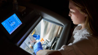 A woman wearing a white lab coat works with a machine that freezes and cuts tissue samples.