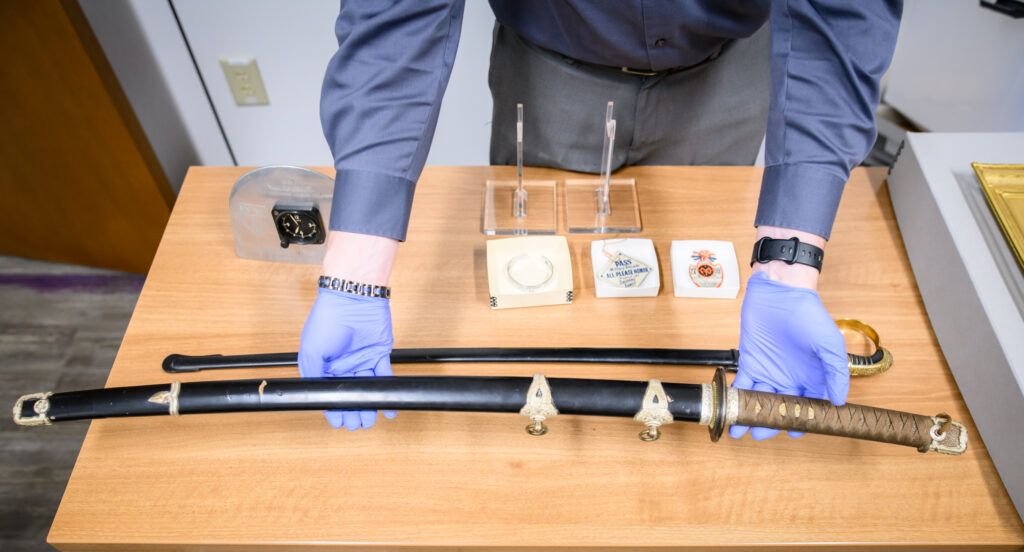 A man holds a sword out above a second sword that's sitting on the table top underneath