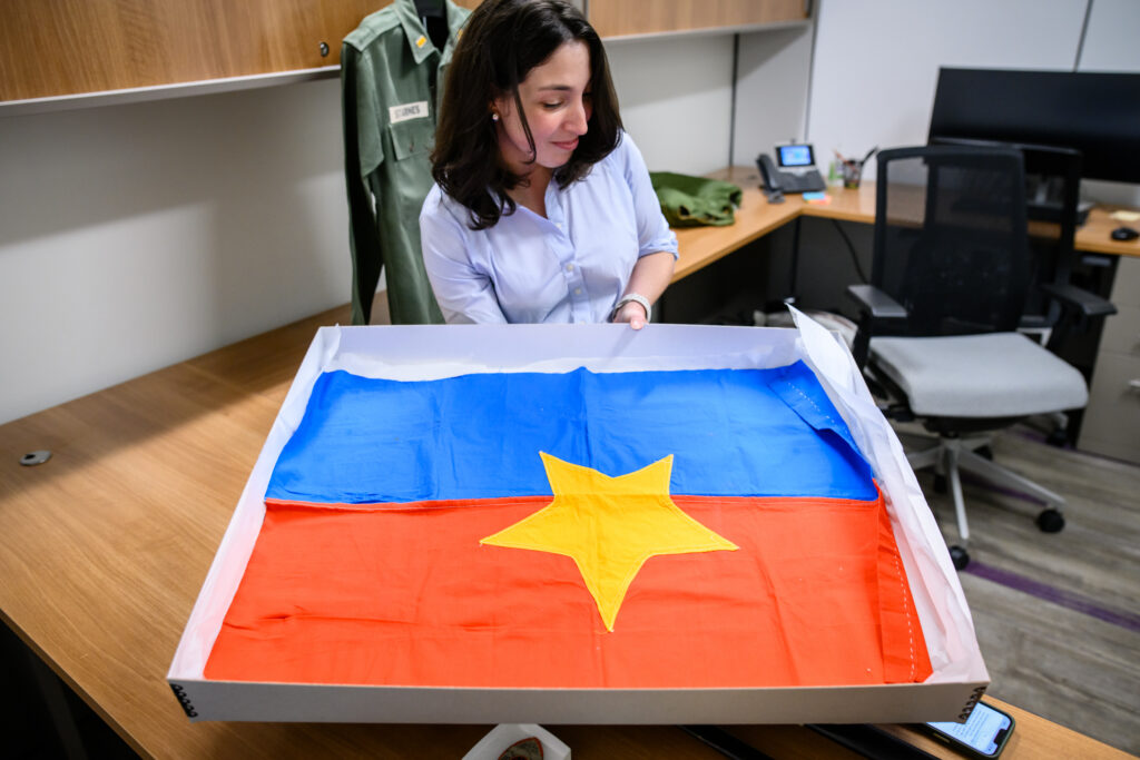 A woman holds a large, flat box with a colorful flag laid out at the bottom of it.