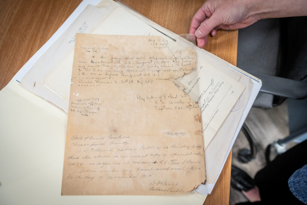 A hand holds the corner of a much-aged and torn paper document with hand-written writing on it.