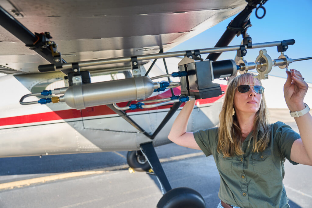 A woman works with a air sampling device on the wing of an airplane.