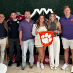 MSSBA students stand in a group in front of a green wall. They are holding a tiger rag in the middle of the photo.