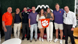 MSSBA students stand in a group in front of a green wall. They are holding a tiger rag in the middle of the photo.