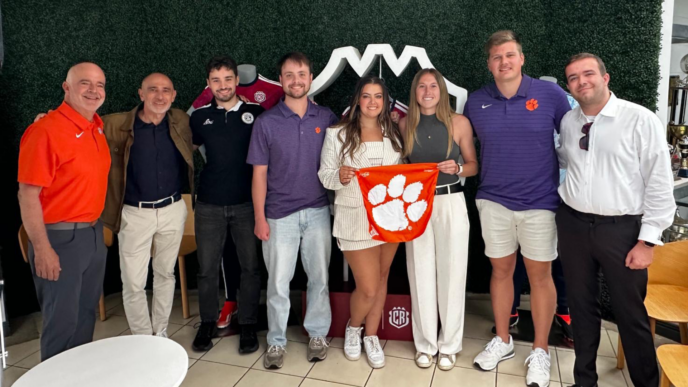 MSSBA students stand in a group in front of a green wall. They are holding a tiger rag in the middle of the photo.