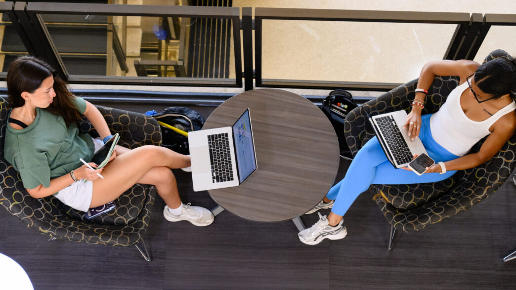 An overhead view of two students lounging in Cooper Library while using their laptops.