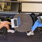 An overhead view of two students lounging in Cooper Library while using their laptops.