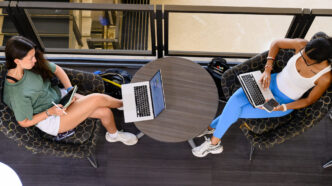 An overhead view of two students lounging in Cooper Library while using their laptops.