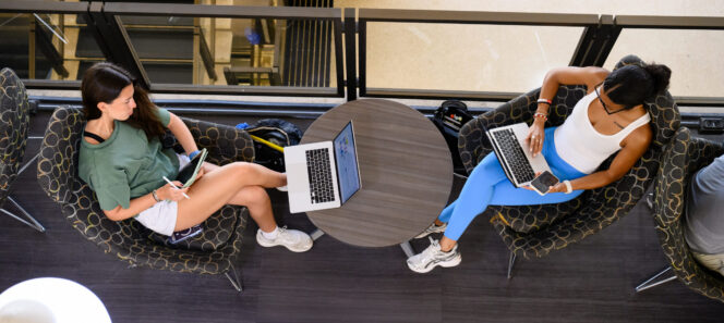 An overhead view of two students lounging in Cooper Library while using their laptops.
