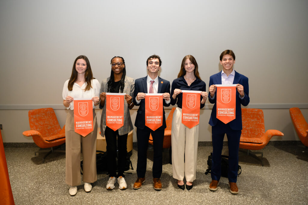 Five students stand holding orange pennants reading Management Consulting Signature Program