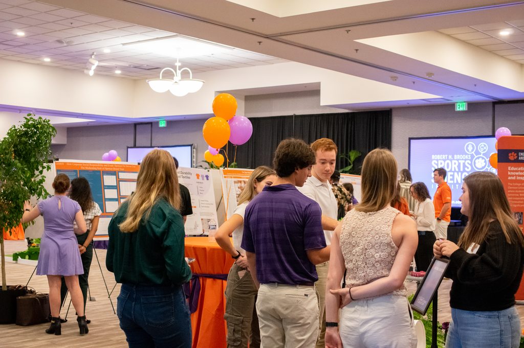 a room full of attendees looking at posters with balloons and large video screens in the background