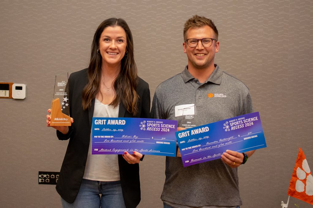 a man and woman are both holding trophies and large-printed checks addressed to them