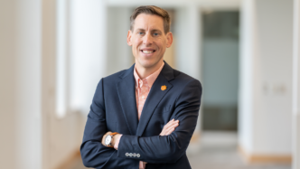 A white man in a pink button up shirt and blue blazer smiles at the camera with his arms folded. Jeremy Vinson, interim director of the School of Accountancy.